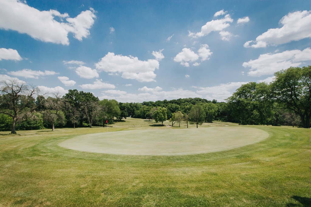 View from behind green with blue skies and rolling hills in the distance