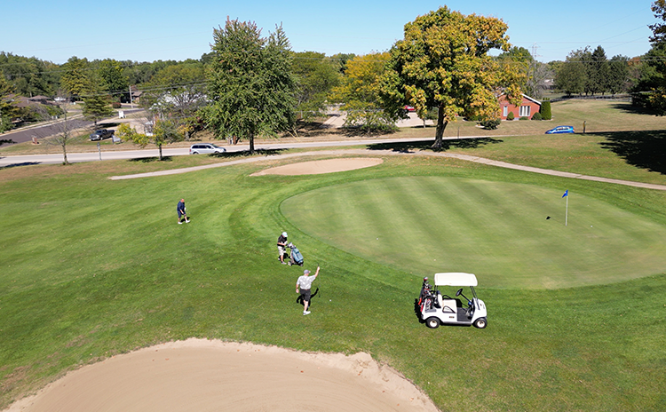 Golfers with golf cart walking across manicured golf course green